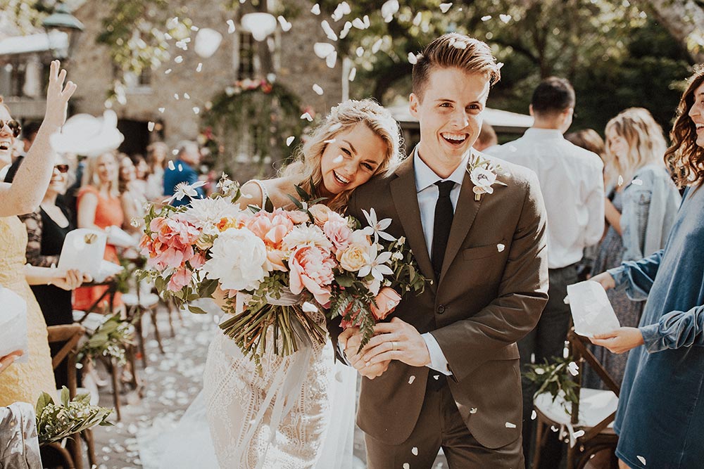 Bride and groom exiting outdoor ceremony with people throwing flower petals