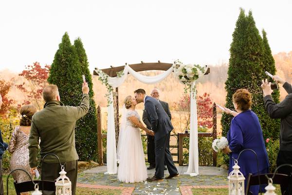 Bride and groom outside under an arch with a few family and friends throwing confetti
