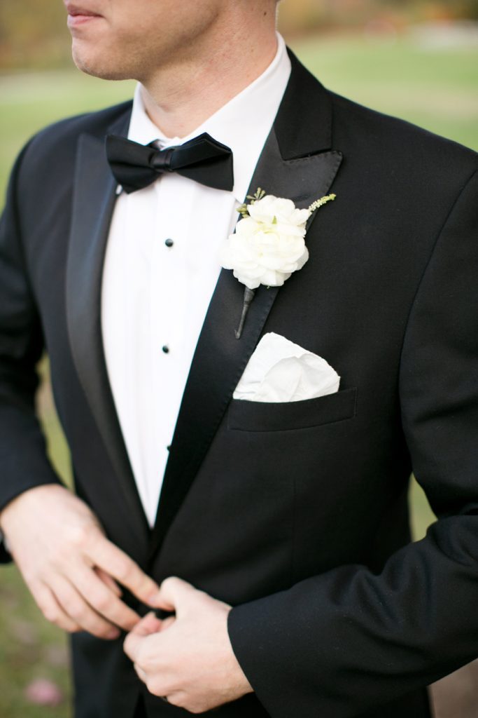 A close up of a man wearing a traditional black tuxedo with a white corsage.