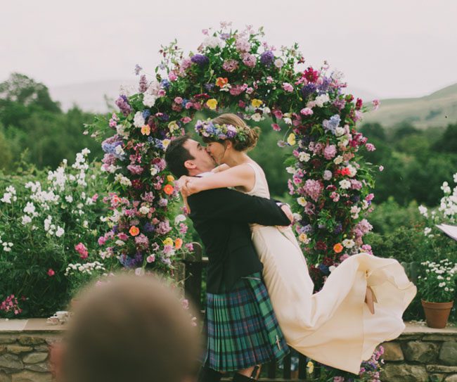 Bride and groom kissing in front of a flower archway