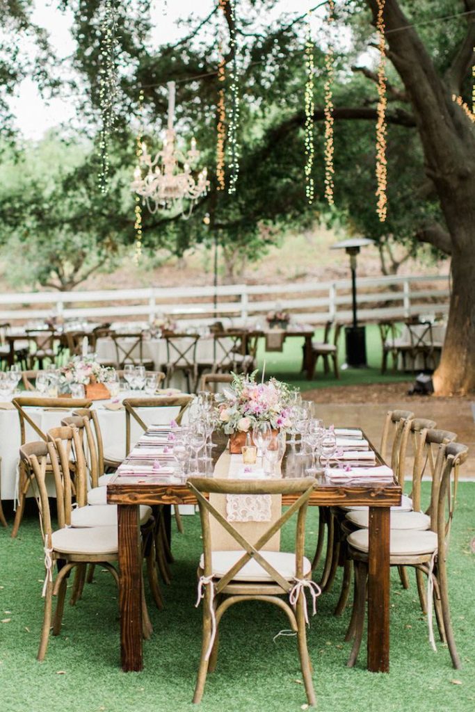 Tables set for a wedding underneath a large tree with strings of white lights hanging from it