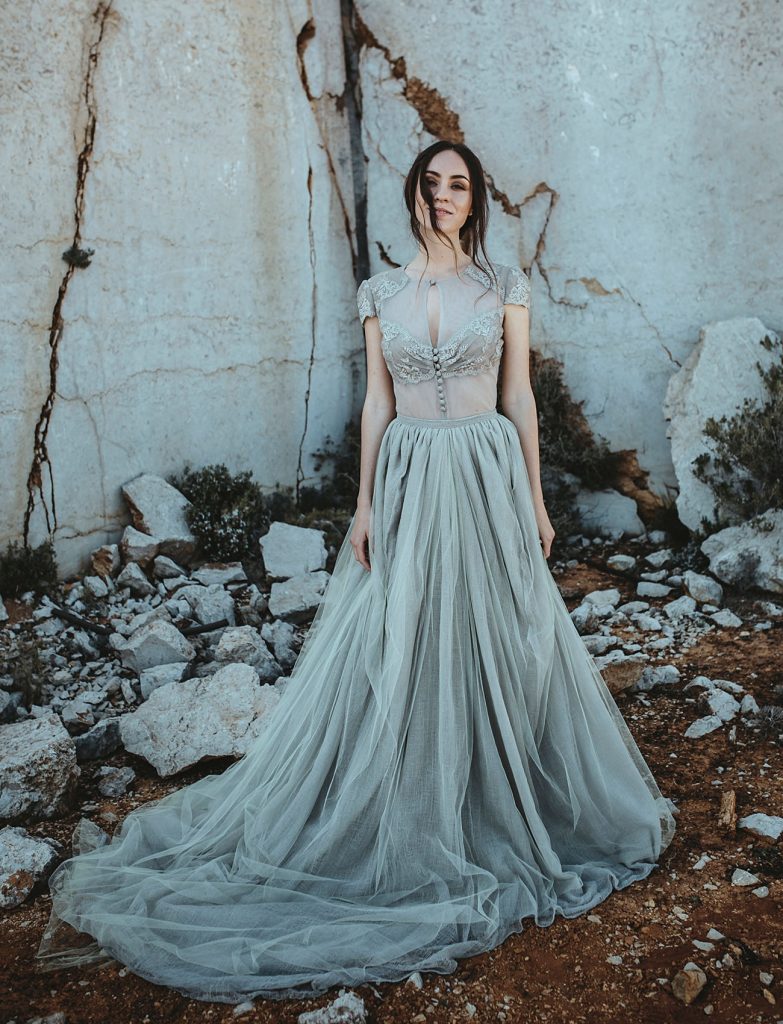 Woman standing in a rock quarry wearing a grey wedding gown with a really full skirt.