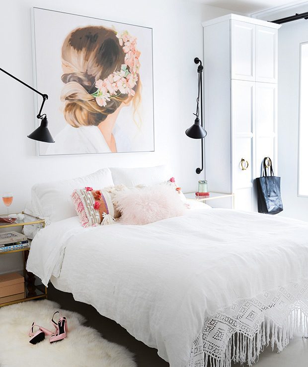 White bedroom with pink pillows and painting of a girl with flowers in her hair above the bed