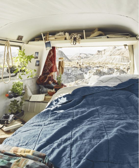 a bed in the back of a VW van, looking out over the wilderness with a navy blue comforter.