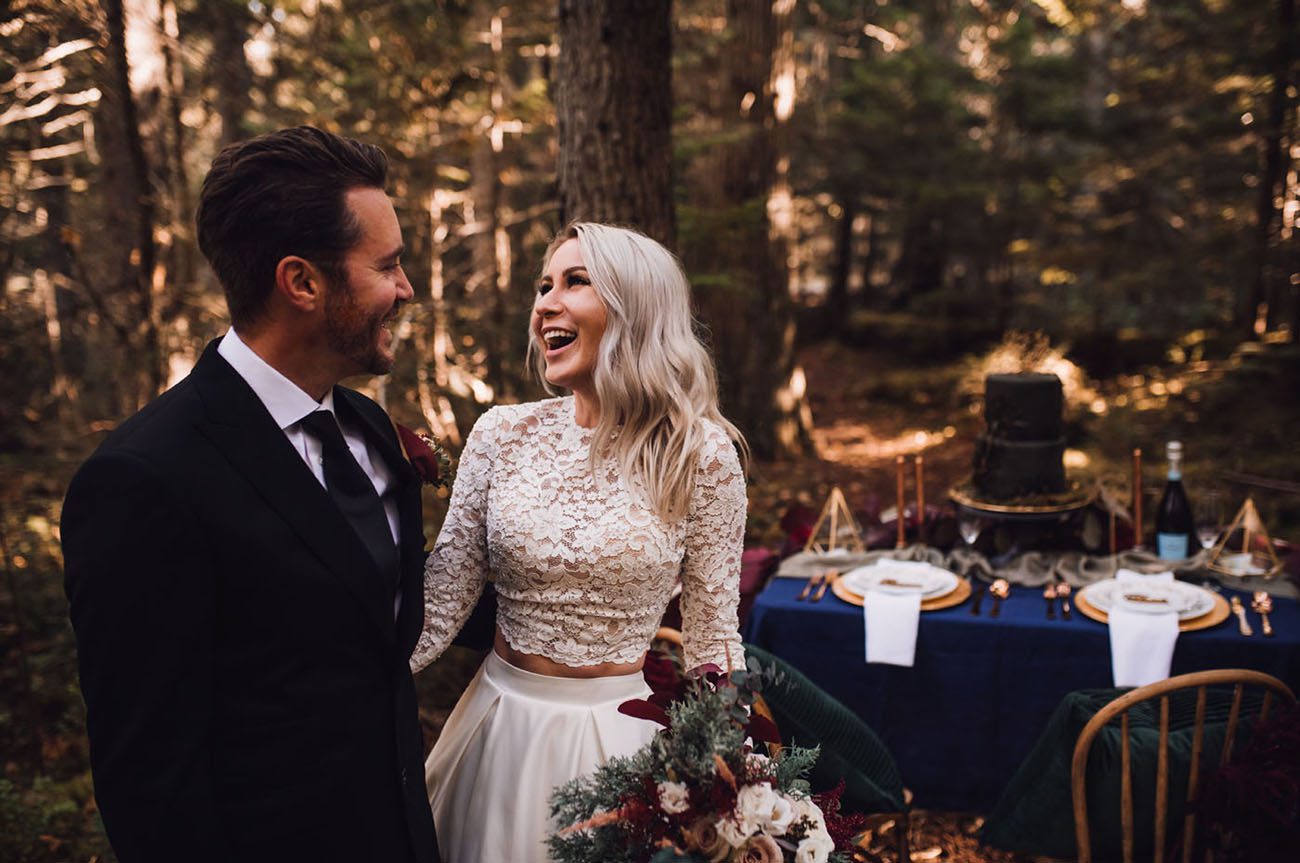 bride and groom standing in the forest. The bride is wearing a two piece dress with a long sleeved lace bodice