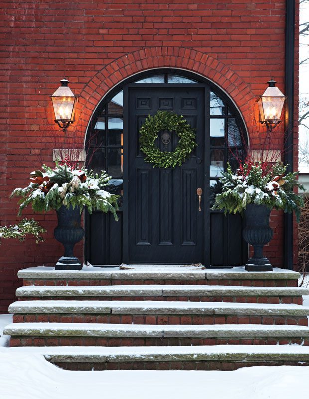 the exterior of a red brick home and a large green leaf wreath and two large planters on either side of the door