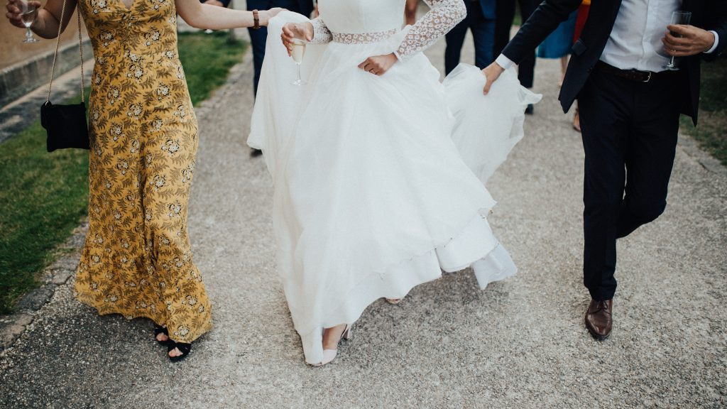 bride walking down the street with groom and friend. You can only see the people from the shoulders down.