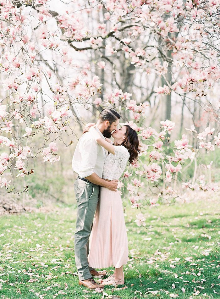 A couple kissing in front of a tree with large pink blossoms