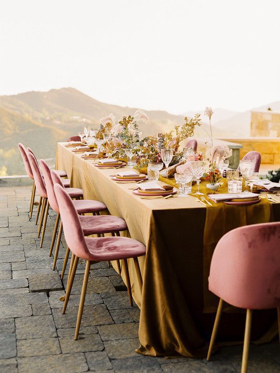 Large pink, orange, and yellow table set for a wedding overlooking mountains and valleys at sunset