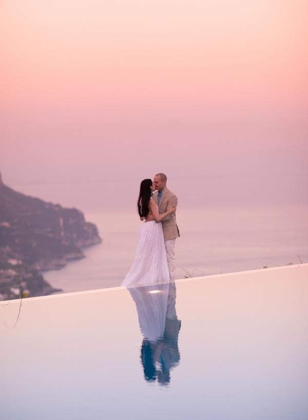 Bride and groom standing on the edge of an infinity pool at sunset