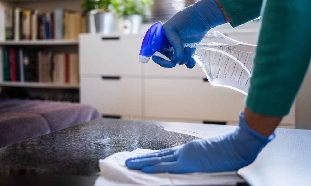 A close-up of someone wearing latex gloves and using bleach to safely disinfect their home. Are you wonder if bleach is safe to clean with? Here's how to use bleach safely around the house to clean during COVID-19.