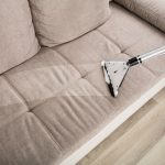 person, using, vacuum, to, clean. beige, couch